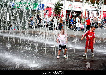 Children in football colours play in fountains in front of Liverpool FC supporters store in Williamson Square Liverpool Stock Photo