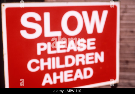 Defocussed red and white sign standing in front of a wooden hut or fence and warning Slow please Children ahead Stock Photo