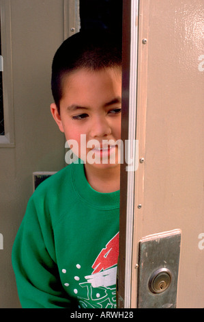 Boy age 7 peeking out of doorway entrance in school classroom. Western Springs Illinois USA Stock Photo
