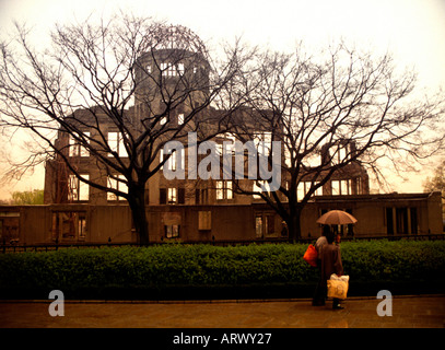 Onlookers stand in the rain beneath umbrellas in front of Genbaku Dome Atomic Bomb Dome in Hiroshima Japan Stock Photo