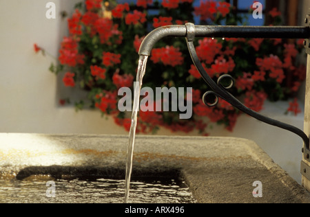 Mountain Village of Guarda Flowing Water Fountain Against Red Flowers Lower Engadine Valley, Switzerlland Stock Photo