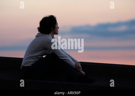 young hispanic woman sitting on a wall looking out at sunset santa cruz tenerife canary islands spain Stock Photo