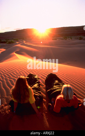 Two people lying in sleeping bags on rippled sand dunes at sunrise as the sun crests over the dunes Stock Photo