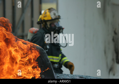 Fire fighter in the background walking around a car fire investigating the situation to prepare to put out the fire. Stock Photo