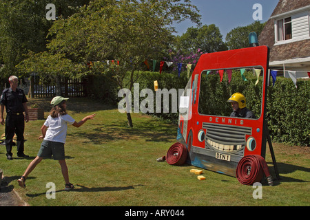 Little girl throwing a wet sponge at fireman at village fete in Findon, West Sussex,UK Stock Photo