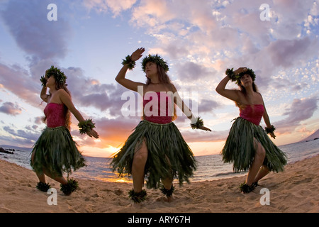 Three hula dancers in ti leaf skirts dance on the beach at sunset at Makena, Maui. Stock Photo