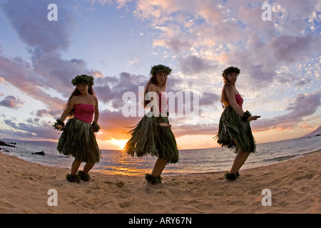 Three hula dancers in ti leaf skirts dance on the beach at sunset at Makena, Maui. Stock Photo