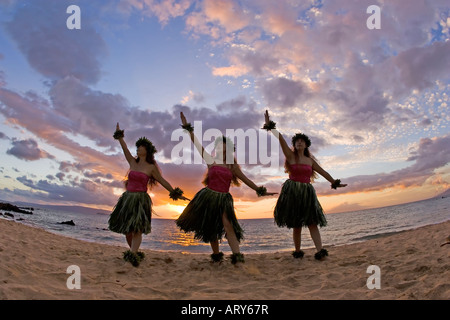 Three hula dancers in ti leaf skirts dance on the beach at sunset at Makena, Maui. Stock Photo