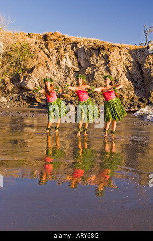 Three hula dancers in ti leaf skirts dance at the water's edge with their reflection at Olowalu, Maui. Stock Photo