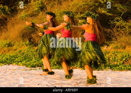 Three hula dancers in ti leaf skirts dance on the beach at sunset at Makena, Maui. Stock Photo