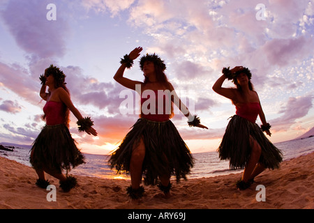 Three hula dancers in ti leaf skirts dance on the beach at sunset at Makena, Maui. Stock Photo