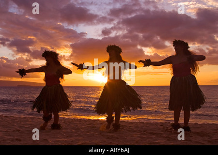 Three hula dancers in ti leaf skirts dance on the beach at sunset at Makena, Maui. Stock Photo