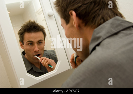 man looking into a bathroom mirror and brushing teeth Stock Photo