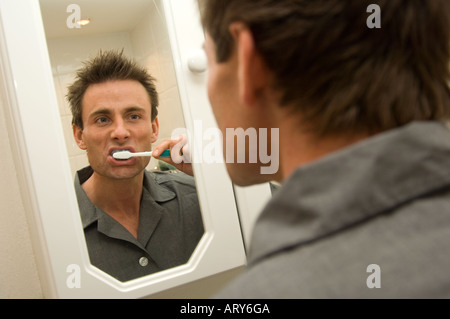 man looking into a bathroom mirror and brushing teeth Stock Photo