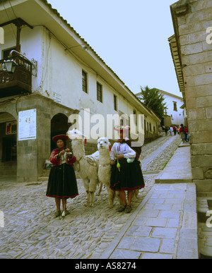 Two indian ladies in traditional dress walking down a cobbled street in Cuzco (Cusco) Peru spinning and leading Llamas Stock Photo