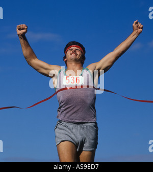 man crossing finish line ribbon at track meet race Stock Photo