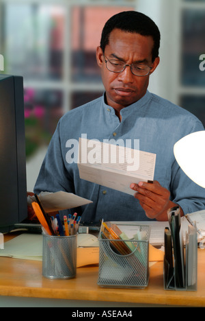 African American man working in a home office and receiving a bill in the mail Stock Photo