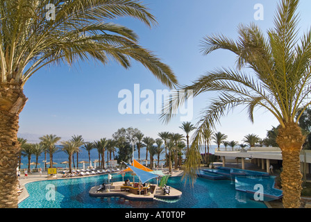 Horizontal wide angle of an empty hotel swimming pool with a swim up bar surrounded by palm trees on a bright sunny day Stock Photo