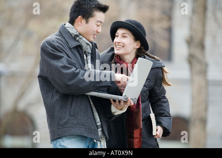 Side profile of a young man using a laptop and a young woman looking at her Stock Photo