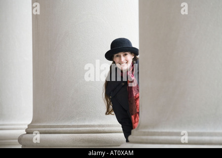 Portrait of a young woman peeking from behind a column and smiling Stock Photo