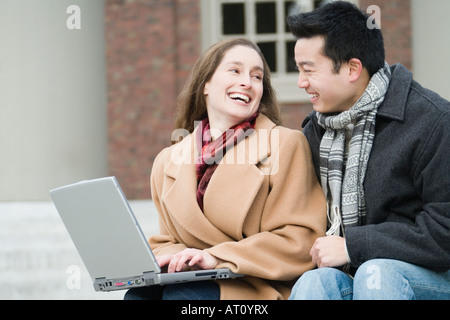Close-up of a young woman using a laptop and smiling with her friend Stock Photo