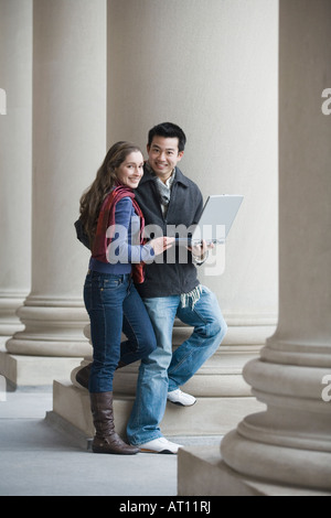 Portrait of a young man holding a laptop and standing with a young woman Stock Photo