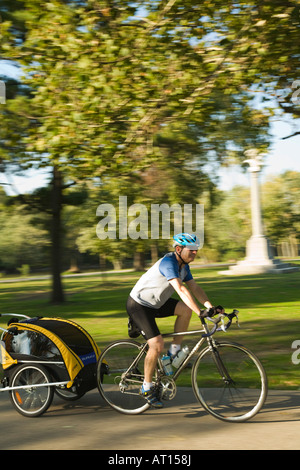 ILLINOIS Geneva Male bicyclist riding bike pulling child carrier on Fox River Trail West paved path through park area Stock Photo