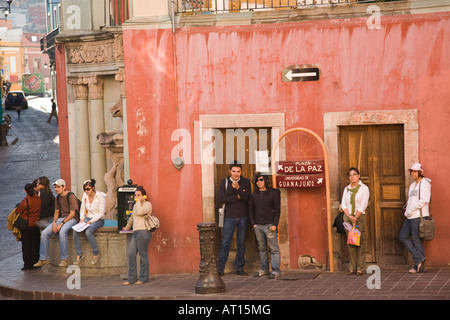 MEXICO Guanajuato University students standing and sitting waiting at bus stop talking pay cellular phones direction sign Stock Photo