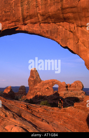Young couple standing in North Window Arch with Turret Arch in  background, Arches National Park, Utah, USA Stock Photo