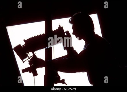 Film Camera Studio still life photographer with 5x4 film camera on tripod stand with lens image plane movement applied, silhouetted against pool light Stock Photo