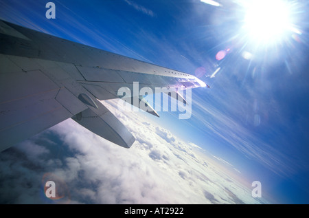 Airplane window view with clouds and sun shining on wing Stock Photo