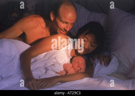 Caucasian father and Asian mother in bed with newborn baby Stock Photo