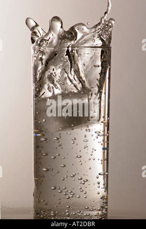 Ice cube dropping into glass of water Stock Photo