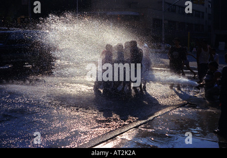 Local Hispanic youths in New York City s Spanish Harlem cool off on a hot summer day in the spray from an opened fire hydrant Stock Photo