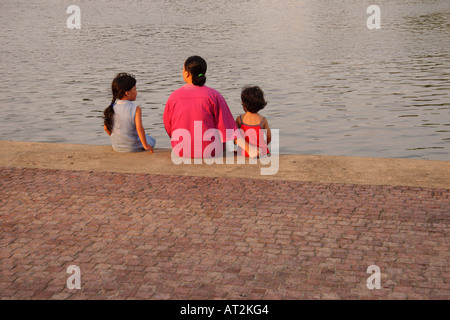 Mother and two daughters sit on the riverbank of Sungai Sarawak, in Kuching, Sarawak, Borneo, Malaysia Stock Photo