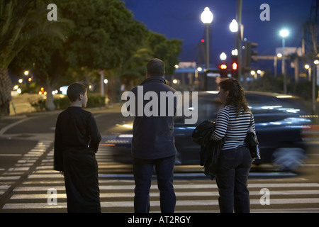 family waiting to cross the road at pedestrian crossing at night during carnaval time in santa cruz de tenerife canary islands Stock Photo