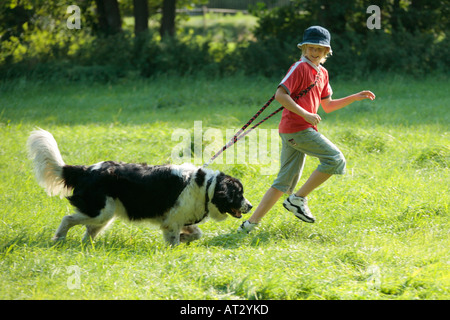 a young boy running across a meadow with his big dog Stock Photo