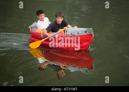 two teenage boys paddling across a lake in an inflatible boat Stock Photo