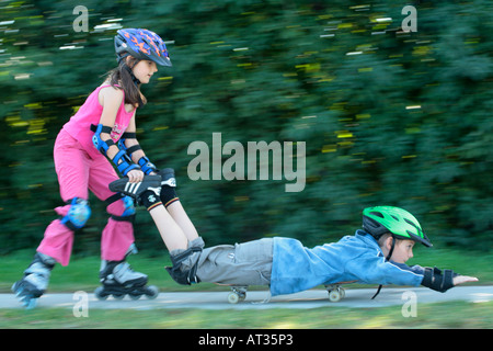 young girl on inlineskates pushing her brother who is lying on a skateboard Stock Photo