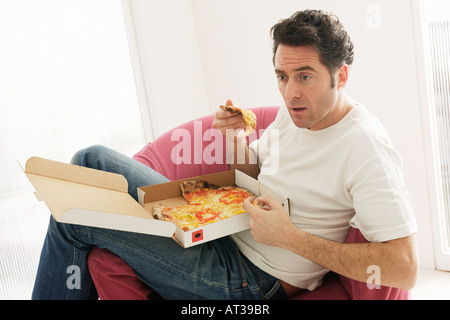 A man sitting in front of a tv eating pizza Stock Photo