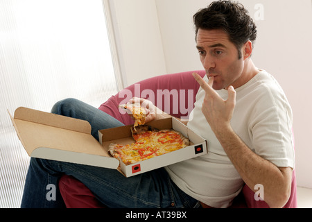 A man sitting in front of a TV eating pizza Stock Photo