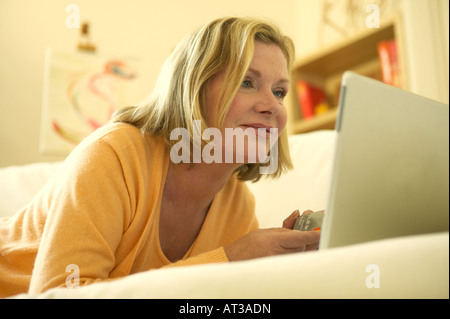A woman lying on a sofa looking at a laptop, holding a credit card Stock Photo