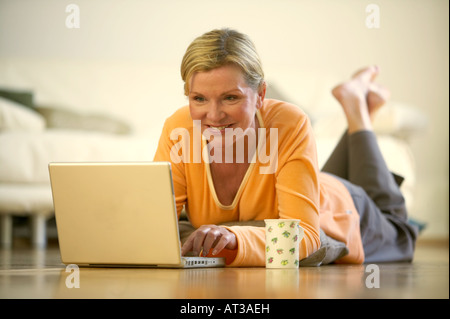 A woman lying on the floor working on a laptop Stock Photo