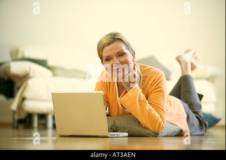 A woman lying on a floor looking at a laptop screen Stock Photo