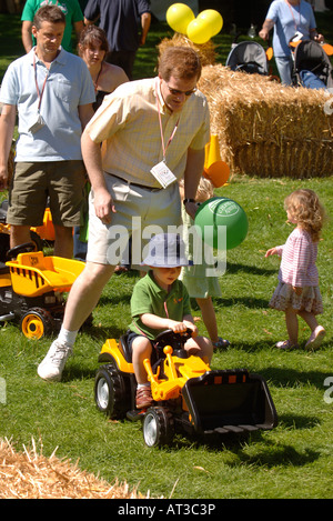PARENTS HELP THEIR CHILDREN PLAY ON TOY DIGGERS A THE INNOCENT VILLAGE FETE IN REGENTS PARK LONDON 2007 Stock Photo