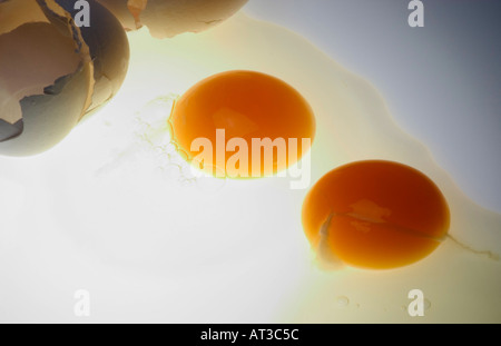 Two broken eggs on bottom lit white surface Stock Photo