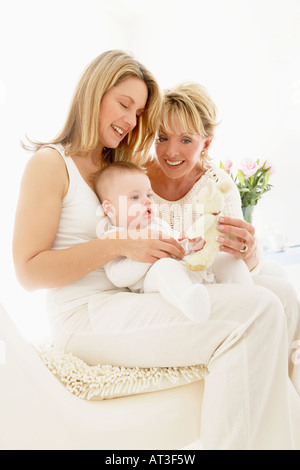 Baby sitting on mother's knee, grandmother holding cuddly toy Stock Photo