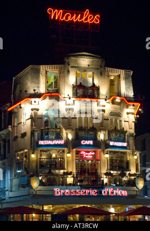 Brasserie d Erlon Restaurant At Night Reims France | REIMS, France — Neon signs spelling "Moules" and "Brasserie d'Erlon" glow above a stepped-gable façade in the Place d'Erlon quarter after dark. Mussels and fries, or moules-frites, remain a signature dish of French and Belgian brasseries, typically served with a choice of white wine, cream, or beer-based broth. The layered awnings for restaurant, cafe, and brasserie sections reflect the building's multi-purpose dining trade. Stock Photo