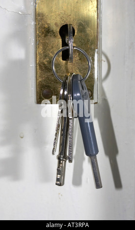 keys on keyring hanging from keyhole in brass lock on a white back door Stock Photo