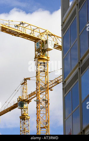 yellow cranes against blue cloudy sky working on construction site near plate glass building in Belfast City Centre Stock Photo
